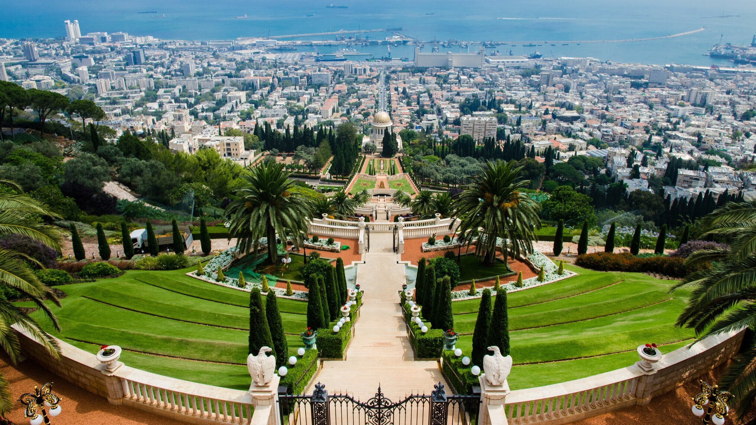 Photograph of Baha'i Gardens, Haifa. A panoramic view of hedge gardens, leading down to the city and beyond to the sea