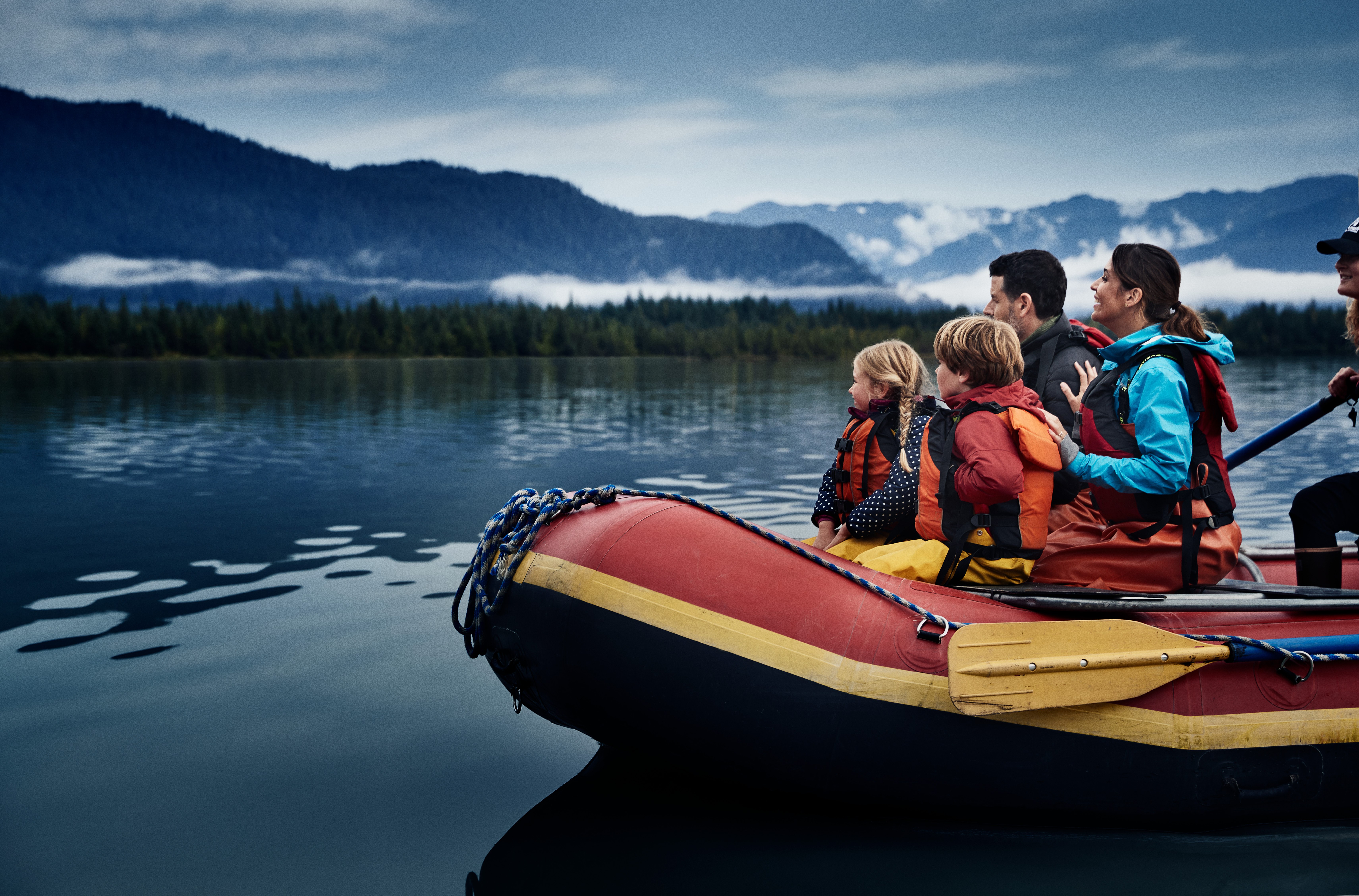 Expedition guests, a family with children, look out on stunning coastline views and deep blue waters from their orange raft