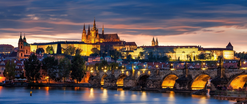 Photograph of Prague lit up at sunset, as seen from a river.