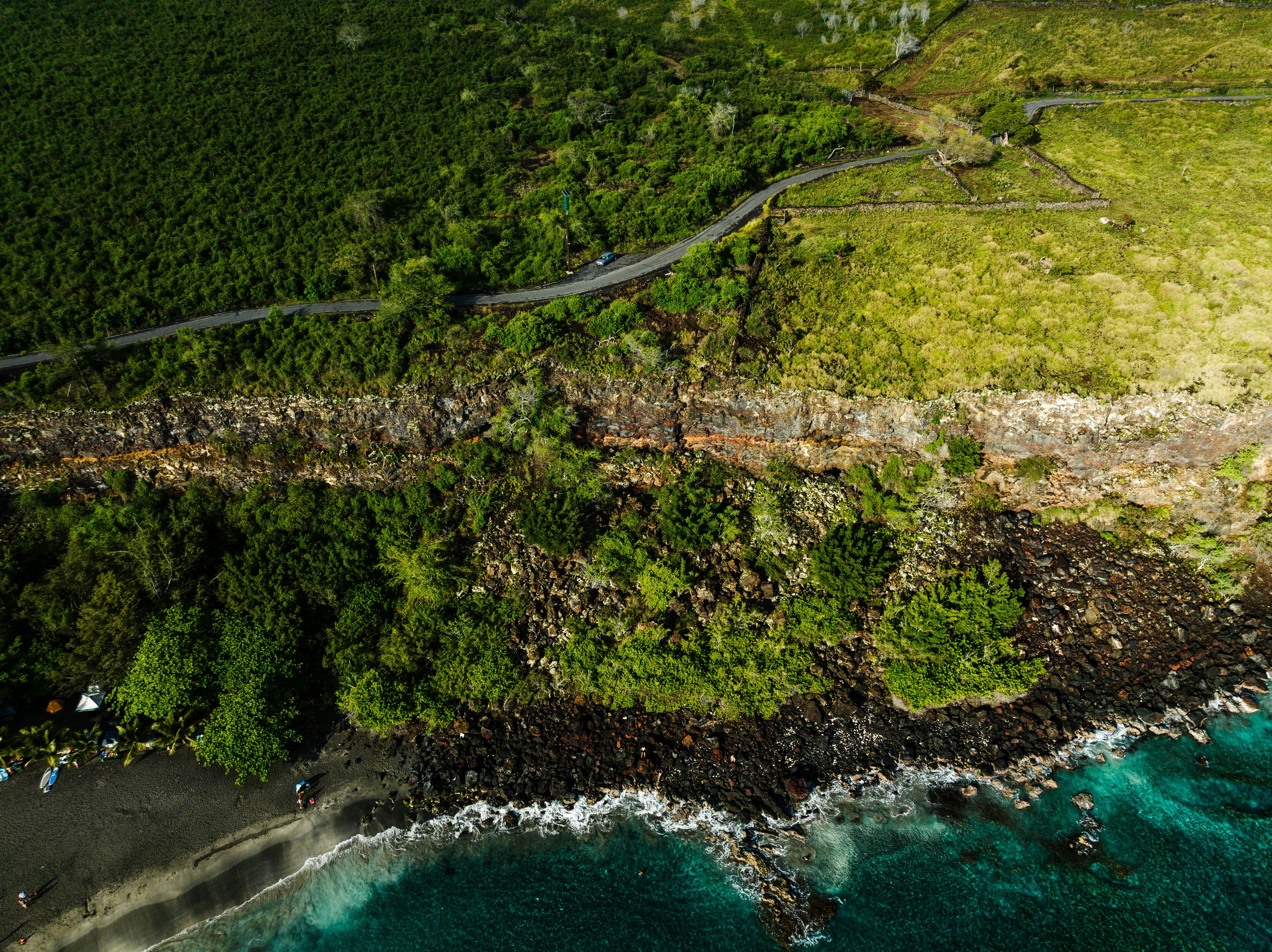 A winding road along a lush green Hawaiian landscape and along jewel toned teal waters