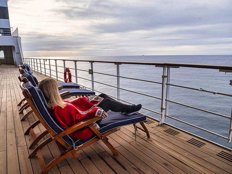 A woman wearing a red blazer lounges in a chair on deck of a Cunard cruise ship