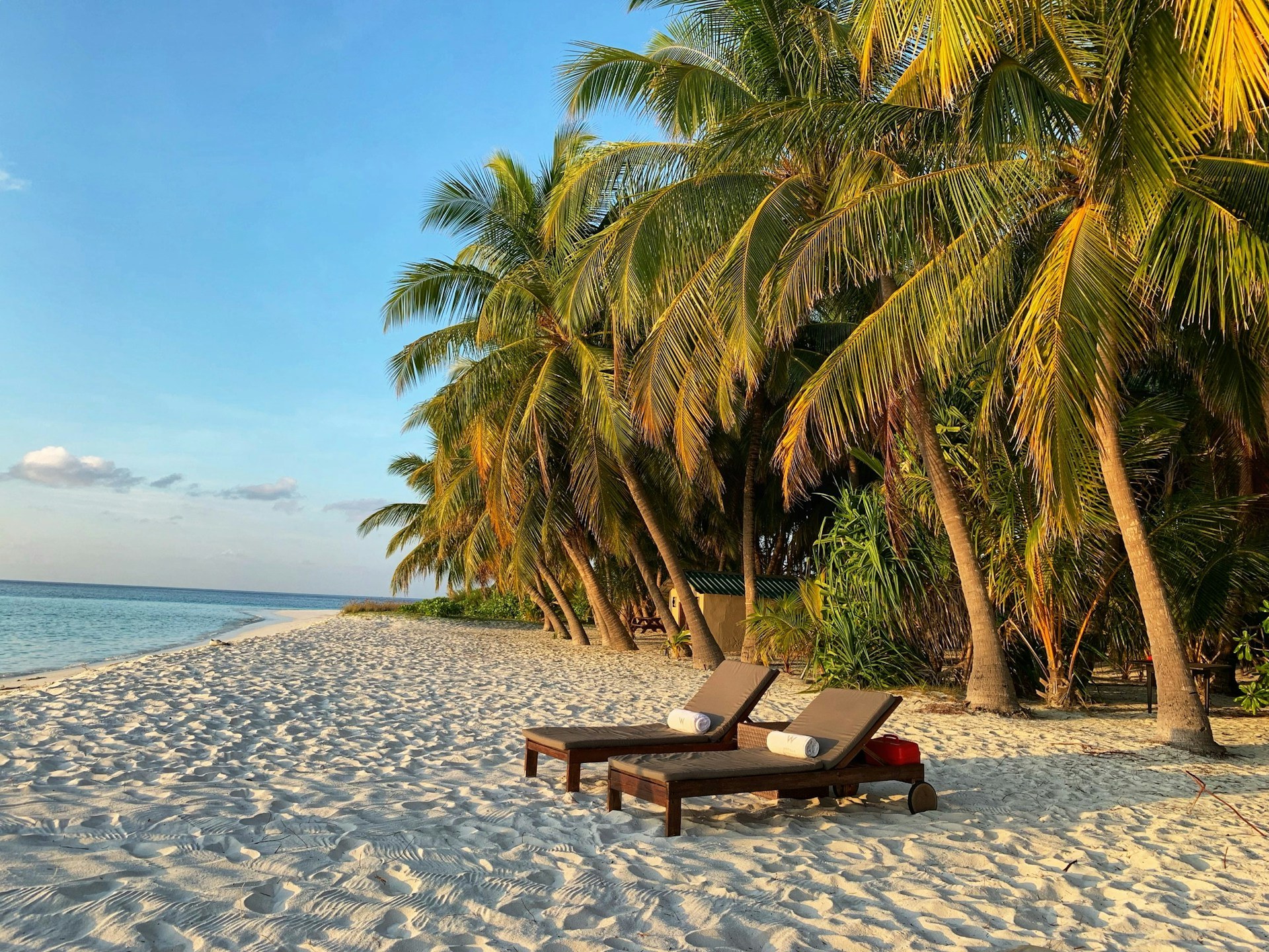 Two wooden lounge chairs sit together on a secluded beach, fresh towels rolled and ready for their occupants.