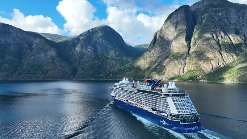 A Celebrity Cruises ship anchors in front of stunning and elevated shoreline scenery