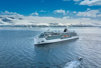 A cruise ship travels through clear waters againt clear polar skies