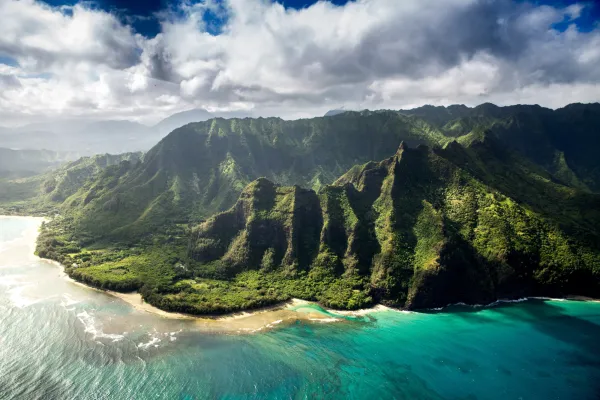 Stunning photography of Hawaii's coastline, lush green elevation against cloudy skies and turquoise waters, taken by photographer Braden Jarvis