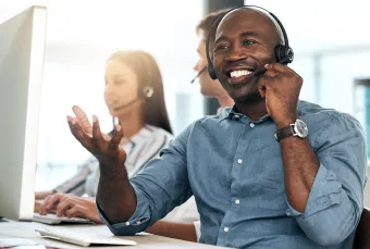A dark skinned service professional smiles as he answers a call on his headset.