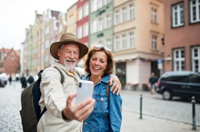 An older couple takes a daytime selfie on the cobblestone streets of a European city.