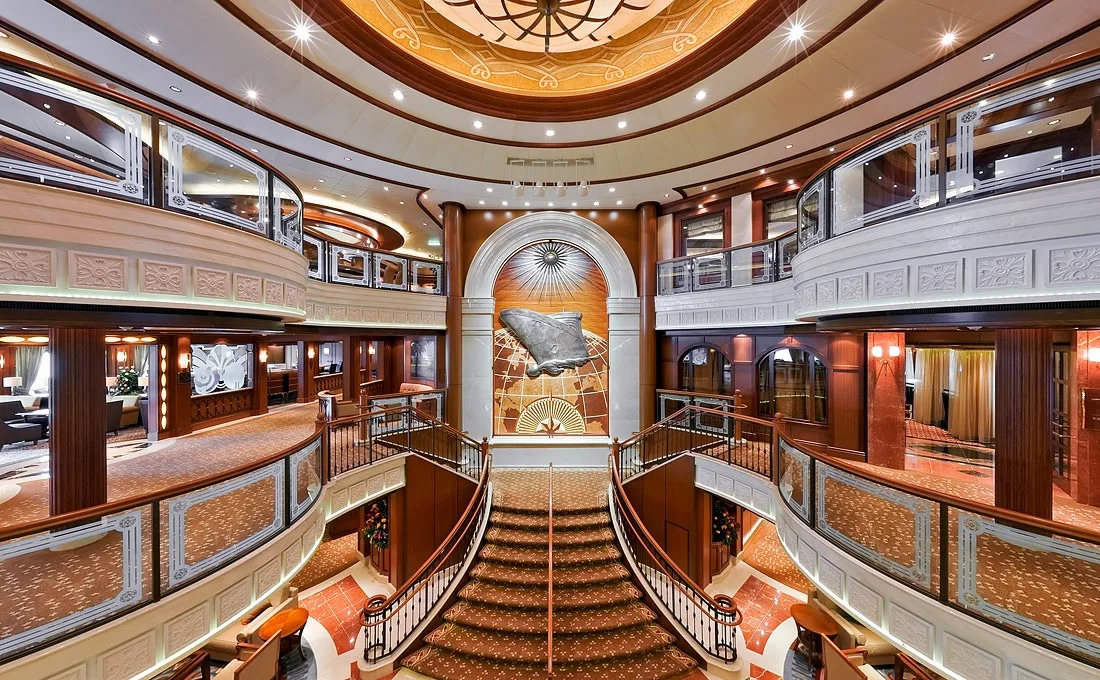 Photograph of the grand lobby on Cunard's Queen Elizabeth. Grand staircases and double balconies create an impressive scene.