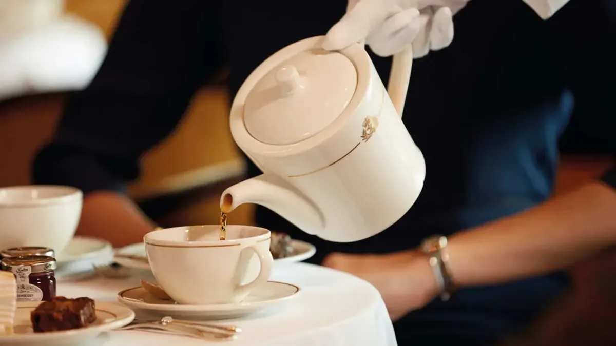 A white gloved hand pours tea from a teapot into a porceilain tea cup during Cunard's signature Afternoon Tea service.