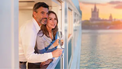 An older couple drink wine as they enjoy the river view from their cruise balcony.