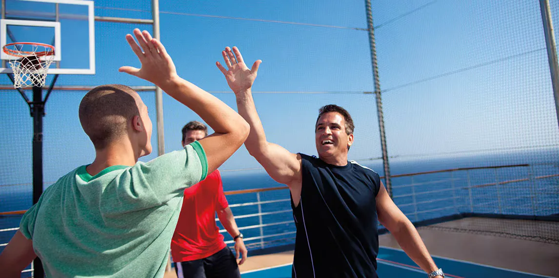 Three men high five on the basketball court aboard a Carnival Cruise ship