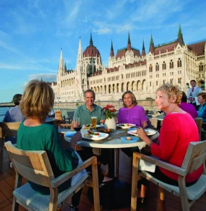 A group of older adults eat lunch on a river terrace