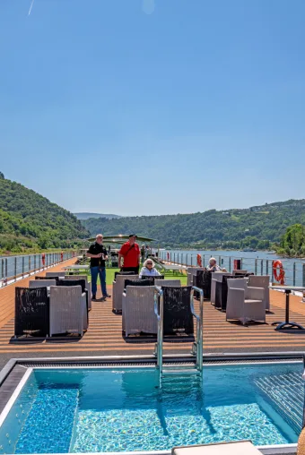 Photo taken from a lounge chair about a sundeck on a cruise along the Rhine River. A pool sits empty and inviting as guests sunbathe on the small deck