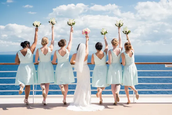 A bridal party poses with bouquets along the railing of a cruise ship at sea
