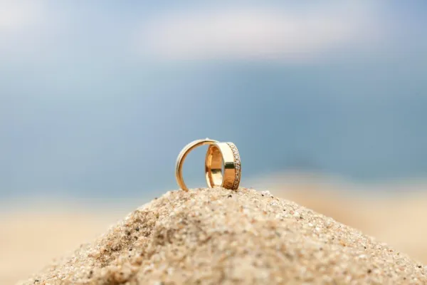 Two wedding rings shine in the sun, on a sandy beach